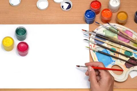 Workplace painter, brush in hand, jars with gouache, canvas for painting Stock Photos