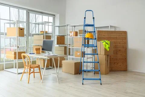 Workplace, stepladder and shelf units with cardboard boxes in warehouse Stock Photos