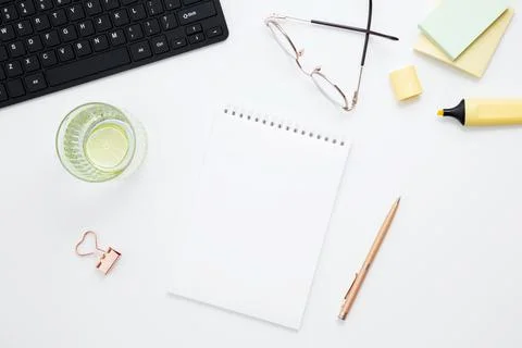 Workplace with white notebook, black keyboard, stationery, glass of water wit Stock Photos