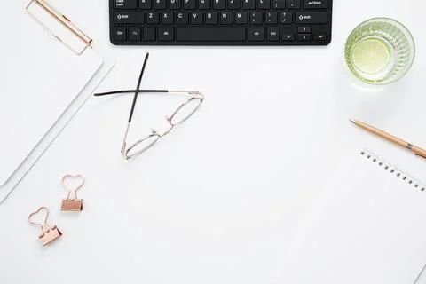 Workplace with white notebook, black keyboard, stationery, glass of water wit Stock Photos