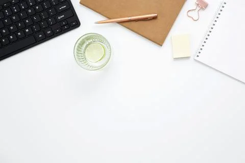 Workplace with white notebook, black keyboard, stationery, glass of water wit Stock Photos