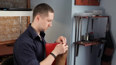 In the workshop, a man is sewing leather workpieces, making a wallet Stock Footage 88839835