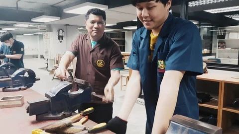Workshop teacher teaching a student how to use tools to hand file a metal Stock Footage 102569986