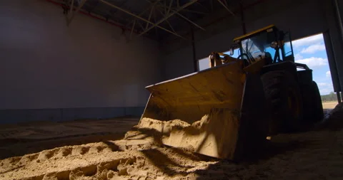 In a workshop under construction, a powerful wheeled tractor evens out the sand  Stock Footage 161983129