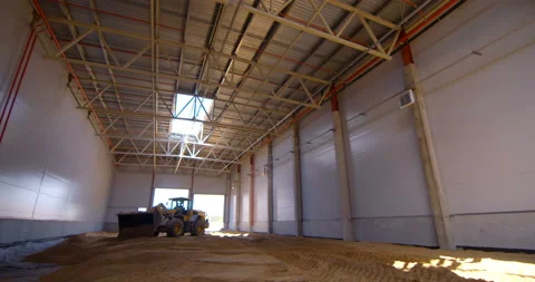 In a workshop under construction, a powerful wheeled tractor evens out the sand  Stock Footage 161983534