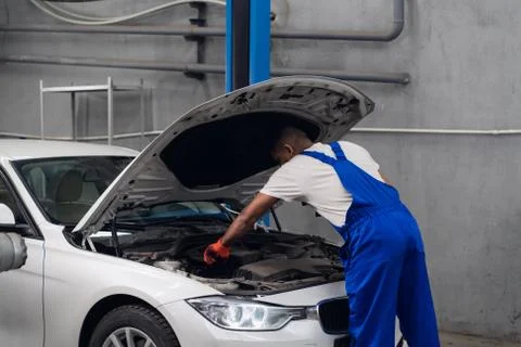 Workshop worker in overalls inspects the car engine Stock Photos