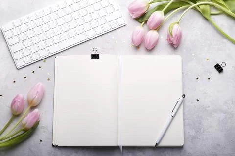 Workspace with keyboard, open diary, pen, paper clips and pink tulips on gray Foto stock