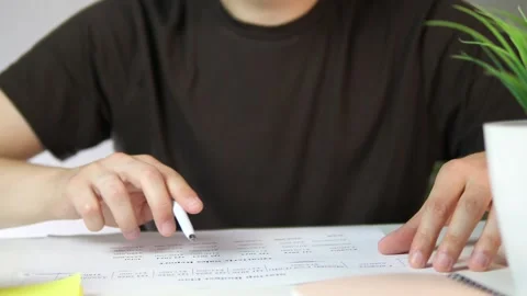 At a workspace, a mans hands in a casual t-shirt carefully examine printed Stock Footage 318212927