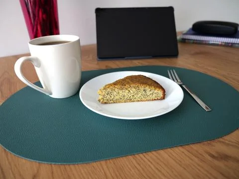 Workspace scene featuring with a cup of coffee, poppy cake, and laptop Stock Photos