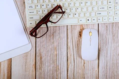 Workspace setup with keyboard, mouse, glasses, pad on wooden table Stock Photos