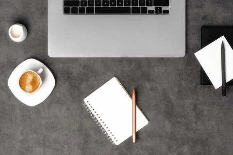 Workspace top view with laptop, notepad, pens and coffee on dark grey stone Stock Photos