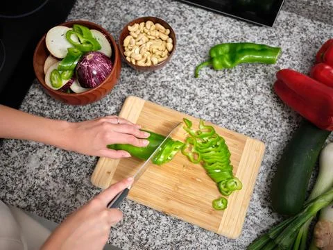 Worktop full of vegetables and the arms of a person cutting a pepper on a board Stock Illustration