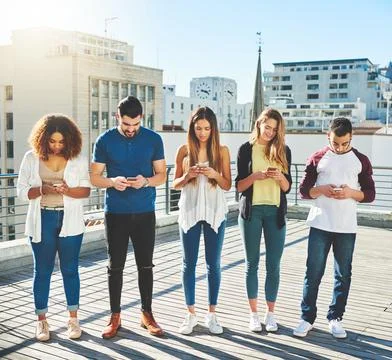 The world is evolving. Full length shot of a group of young people texting on Stock Photos