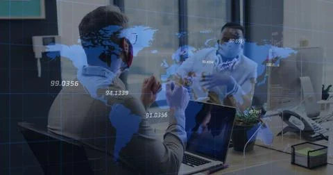 World map over two diverse male office colleagues wearing face masks discussing Stock Photos