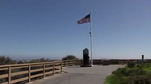World War II bronze statue below american flag in strong wind on cliff. Stock Footage 67556084