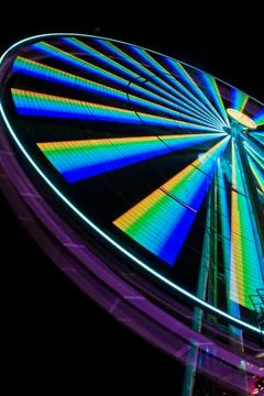 Worm's eye view of a ferris wheel lit up at night with yellows greens blues and 写真素材