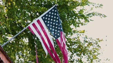 Worn American flag with torn stripes hanging from pole in afternoon light Stock Footage 321324935