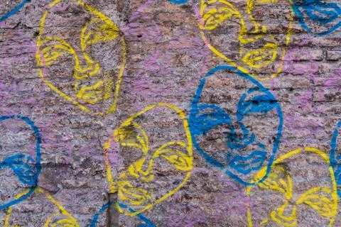Worn brick wall with graffiti faces background texture. Stock Photos