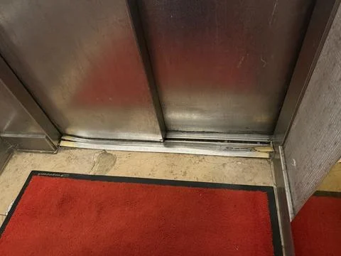 Worn elevator door with visible floor damage and red carpet in building ent.. Stock Photos