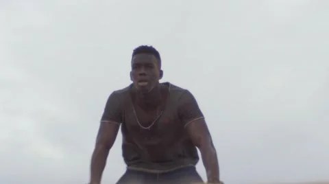 Worn-out black guy kneeling down on a desert sand Video stock 67559253