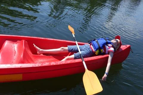 Worn out, child lying down in canoe on a hot summers day; Stock Photos