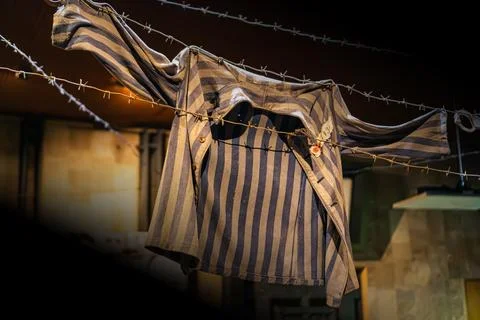Worn prison uniform hanging on barbed wire fence, fastened with buttons, show Stockfoto's