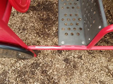 Worn red metal play structure and brown mulch Stock Photos
