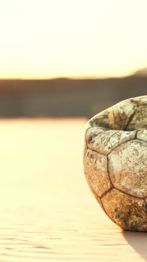 A worn soccer ball lies on a sandy beach as the sun sets on the horizon Stock Footage 337943953