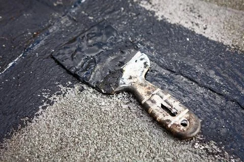 Worn spatula with dried black mastic on a rooftop surface Photos