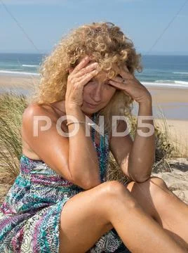 Worried blond girl on the beach sitting on the sand Stock Photos