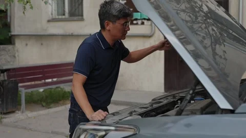 Worried car owner looking under open hood of SUV outdoors Stock Footage 342627984