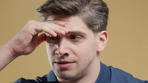 Worried man biting his lips with restless eyes in a studio portrait. Yellow back Stock Footage 340425098
