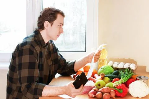 Worried man checking a long receipt next to groceries, illustrating high fo.. Foto stock