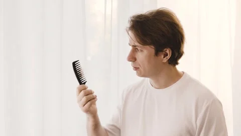 Worried man examines a comb with fallen hair. This male grooming concept shows a Stock Footage 337546366