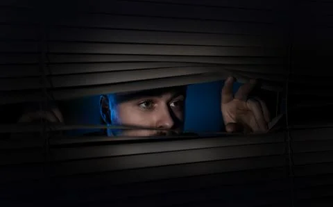 Worried man looking through window blinds into darkness. Paranoia concept Stock Photos