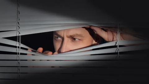 Worried man looking through window blinds into darkness. Paranoia concept Stock-Fotos