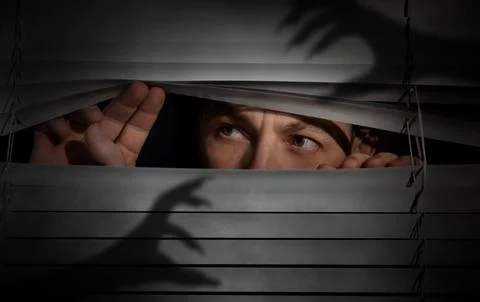 Worried man looking through window blinds into darkness. Shadow of hands wi.. Stock Photos