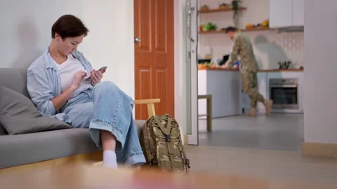 Worried mother sitting with smartphone while soldier and child interact Stock Footage 340340288