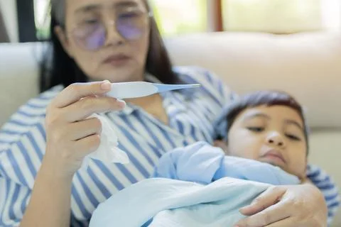 Worried mother using thermometer while checking her little son by temperatu.. Stock Photos