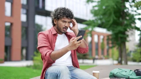 Worried young man read bad news on mobile phone while sitting on a bench  Stock Footage 302473159