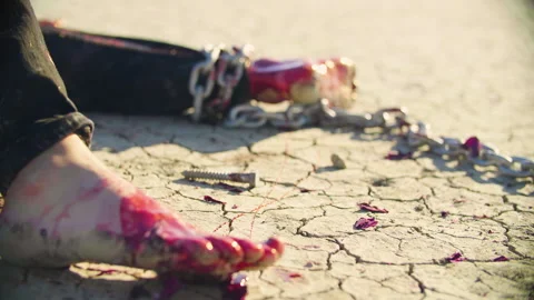 Wounded bleeding man, shackled by the ankle, lies on dry scorched earth Stock Footage 293113868