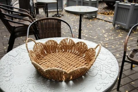 A woven basket placed on a round table outdoors during a rainy day at a cafe 스톡 사진