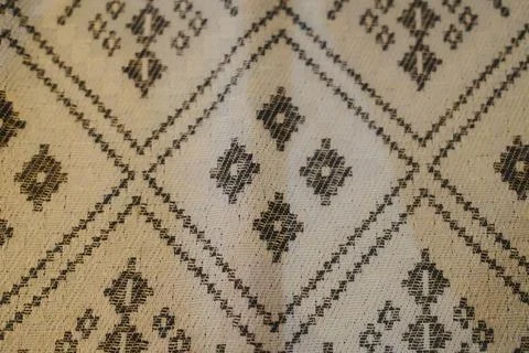 The woven cloth features complex geometric and diamond patterns in a beige Stock Photos