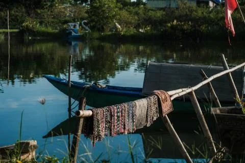 Woven mats drying on a bamboo rack next to a blue wooden boat on a river Stock-Fotos