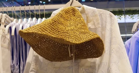 Woven straw sun hat hanging on clothing rack inside fashion retail store Stock Footage 314466624