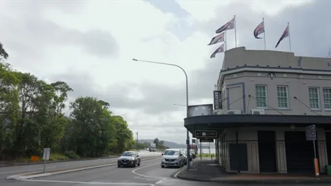 Woy Woy pub hotel with flags on roof beside curved road with passing cars Stock Footage 333520171