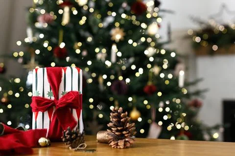 Wrapped Christmas Present Box with Red Bow on Table against Christmas Tree .. Stock Photos