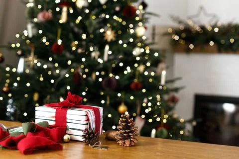 Wrapped Christmas Present with Red Bow on Wooden Table against decorated tr.. 库存照片
