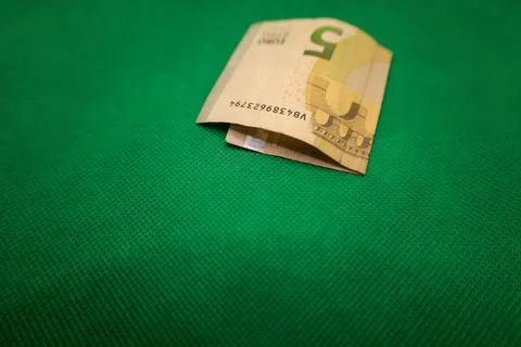 Wrapped five-euro note resting on a vibrant green surface, showcasing its u.. Stock Photos