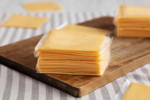 Wrapped Yellow Cheddar Cheese in a Stack on a wooden board, side view. Clos.. Stock Photos